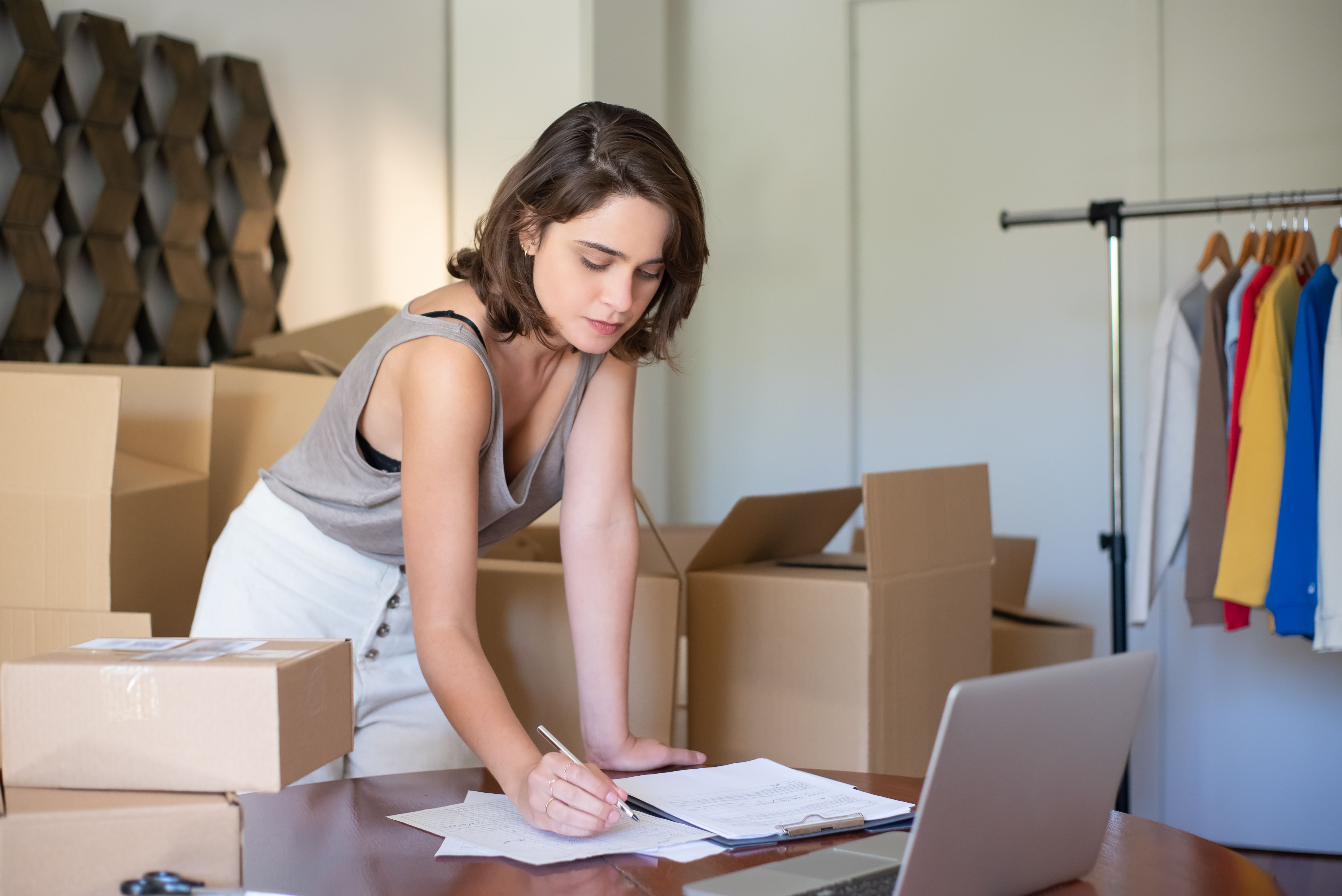 Woman entrepreneur writing beside boxes and a laptop