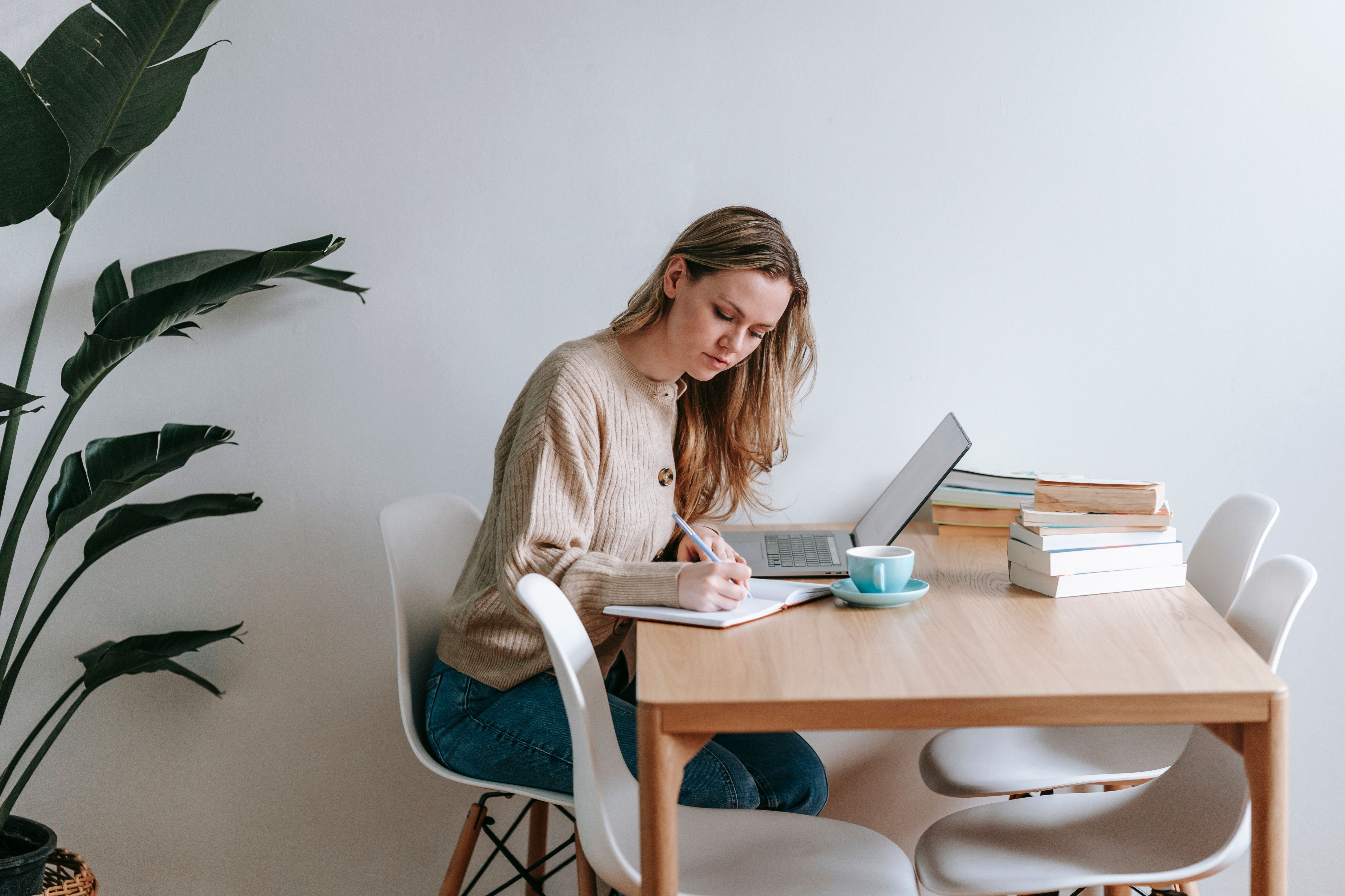 Woman writing in a notebook beside a laptop